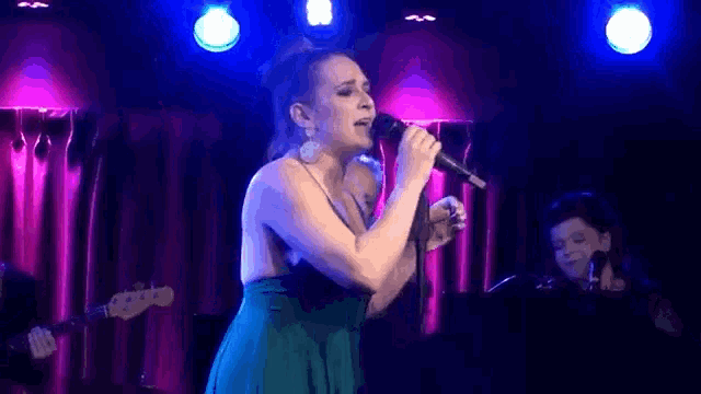 a woman in a blue dress is singing into a microphone on stage .