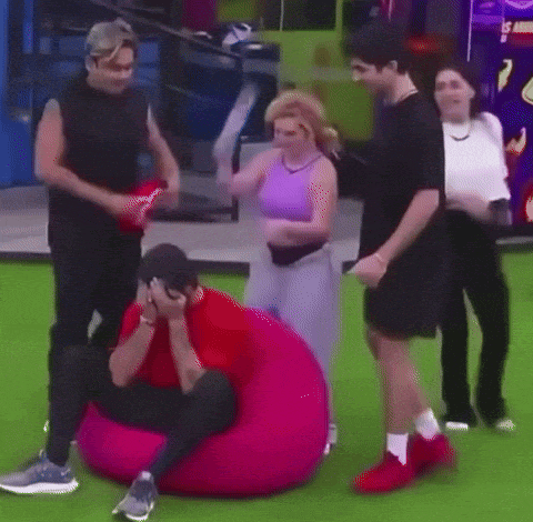a group of people are standing around a man who is sitting on a pink bean bag chair .