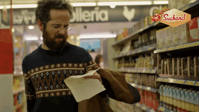 a man in a sweater is looking at a piece of paper in a supermarket