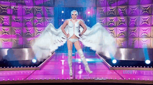 a drag queen is walking down a runway wearing a white angel costume and white boots .