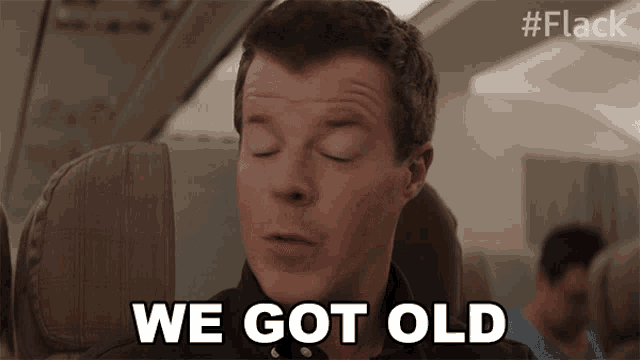 a man sitting on an airplane with his eyes closed says we got old