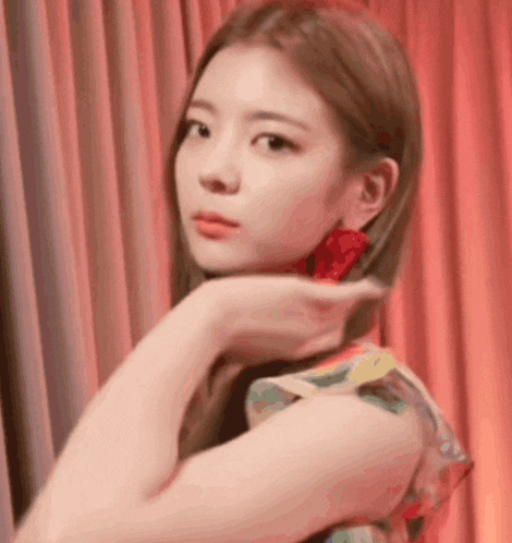 a woman in a floral dress is standing in front of a red curtain and touching her hair .