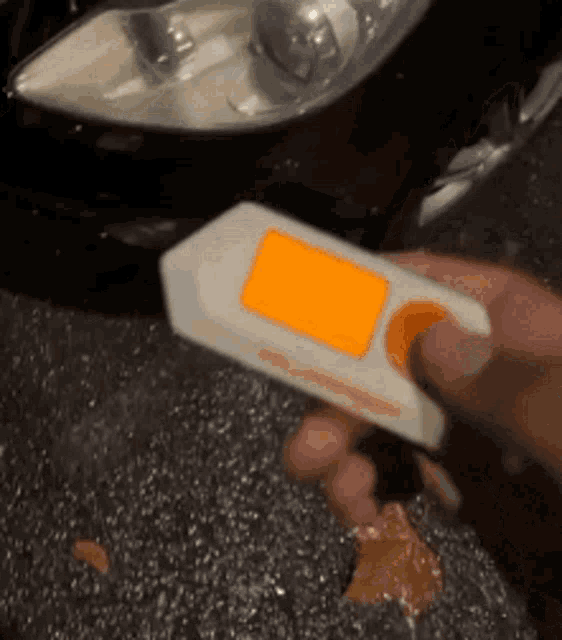 a person is holding a remote control in their hand in front of a car headlight .