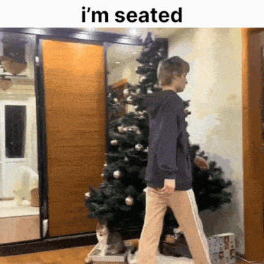 a person standing in front of a christmas tree with the words i 'm seated on the bottom