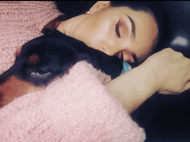 a woman in a pink sweater sleeping with a dog