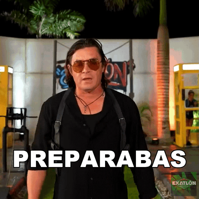 a man wearing sunglasses and a black shirt is standing in front of a sign that says preparabas