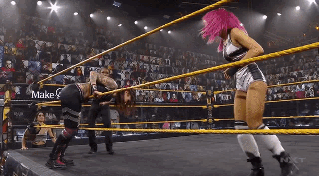 a woman with pink hair is in a wrestling ring with a sign that says make you