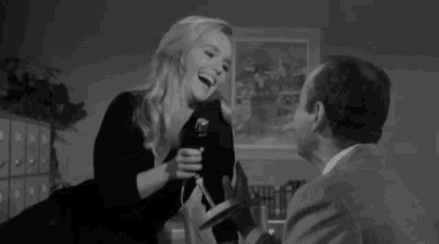 a woman is smiling while holding a microphone in front of a man in a suit .
