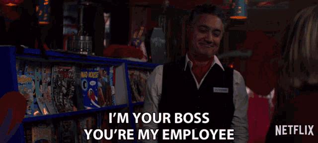a man in a vest says " i 'm your boss you 're my employee " in front of a shelf of magazines