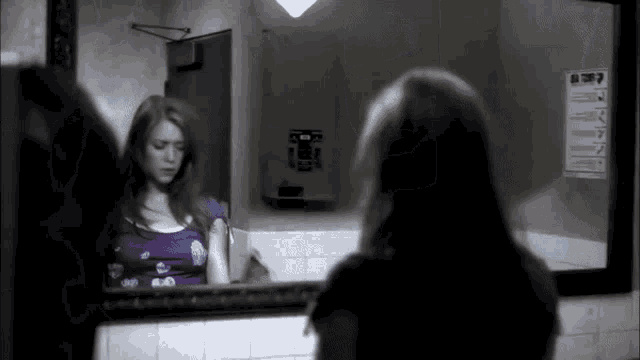 a black and white photo of a woman looking at her reflection in a mirror