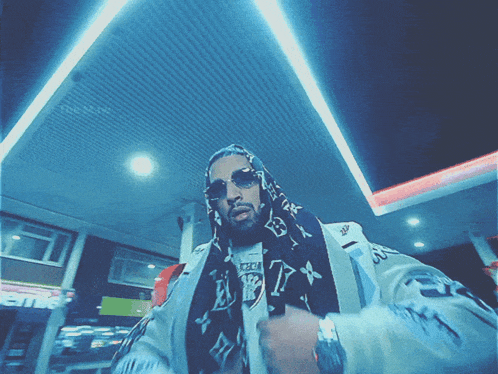 a man wearing sunglasses and a scarf with a louis vuitton logo on it stands in a gas station