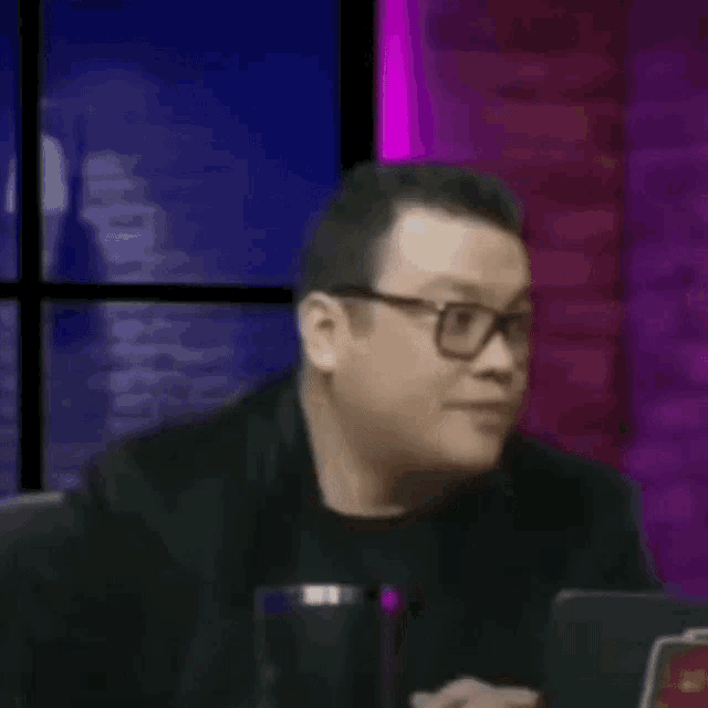 a man wearing glasses is sitting at a table with his hands on his face .