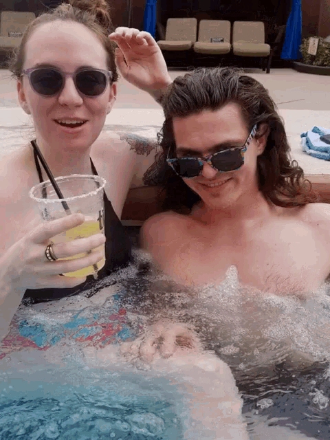 a man and a woman in a hot tub holding drinks and smiling