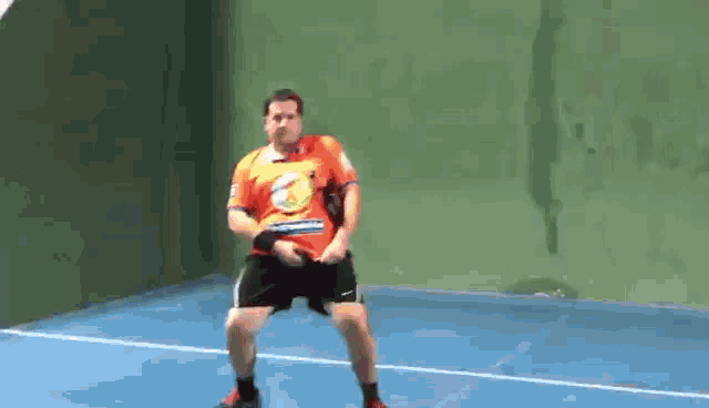 a man in an orange shirt is dancing on a blue court