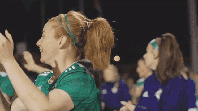a woman wearing a green adidas shirt is clapping