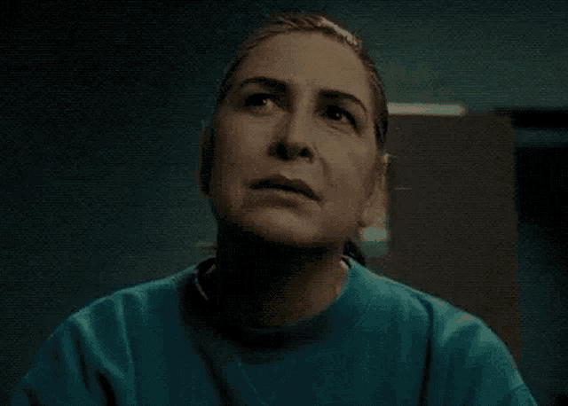 a woman in a blue sweatshirt is looking up at the sky in a dark room .