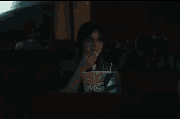 a woman is eating popcorn while watching a movie in a dark theater