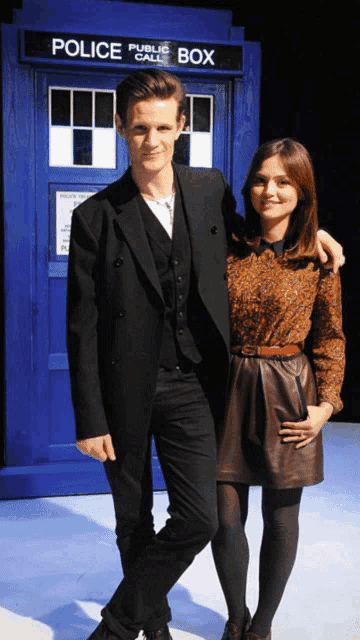 a man and a woman stand in front of a blue public call box