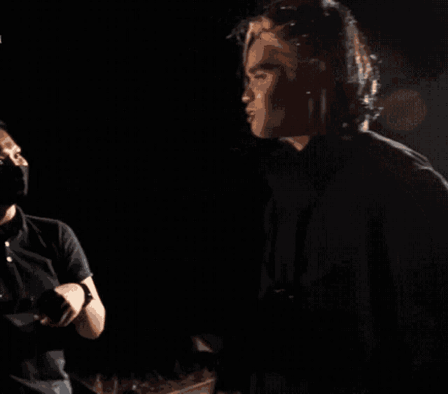 a man in a black shirt is giving a high five to another man in a dark room .