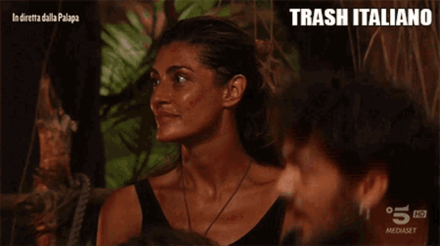 a woman in a black tank top looks at a man in a black shirt with trash italiano written below her
