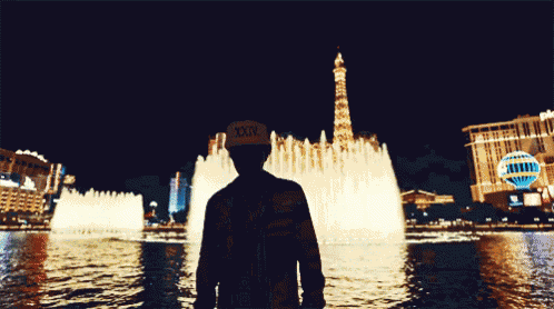 a man stands in front of a fountain wearing a hat that says xxl