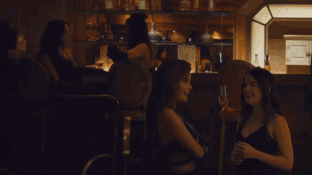 two women are sitting at a bar talking to each other and one is holding a glass of wine