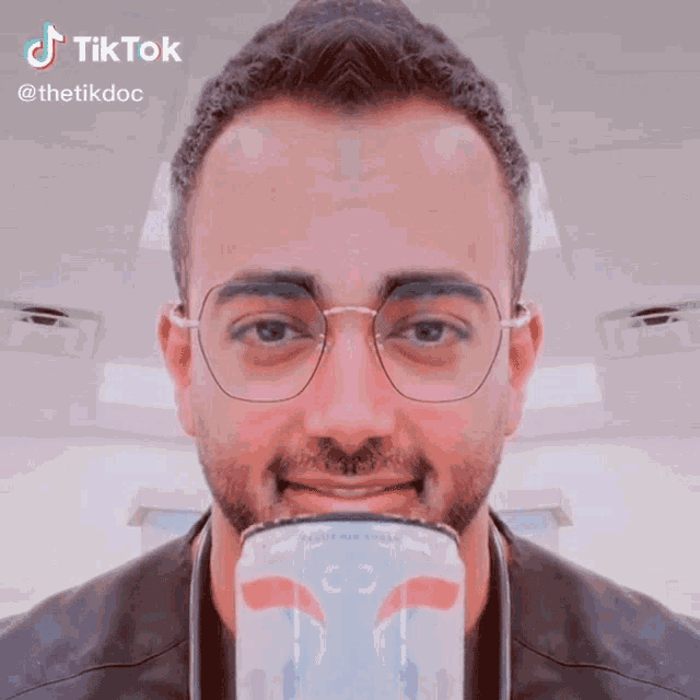 a man with glasses is holding a can of pepsi in his mouth