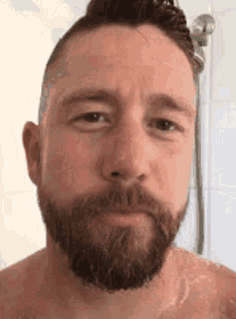 a shirtless man with a beard is taking a shower in a bathroom .