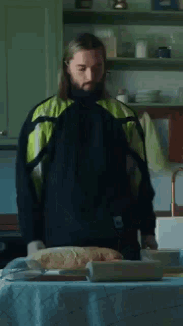 a man with long hair and a beard is standing in a kitchen .