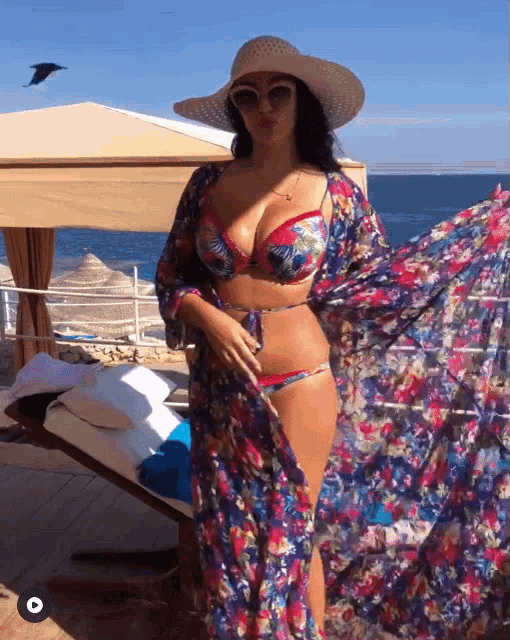 a woman wearing a bikini and a floral dress is standing on the beach