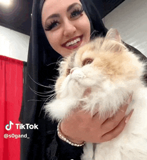 a woman in a black hijab is holding a fluffy cat in her arms .