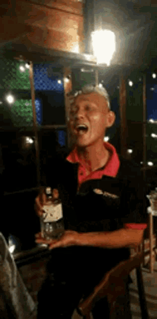 a man in a red shirt is holding a bottle of alcohol and laughing