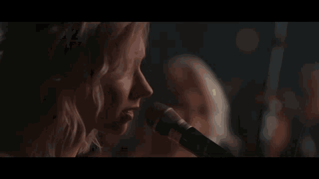 a woman is singing into a microphone with a blurry background