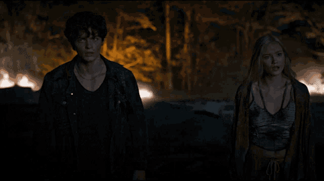 a man and a woman are standing in a dark forest at night