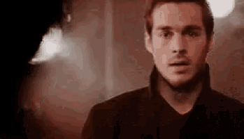 a man in a black shirt is standing in a dark room with smoke coming out of his mouth .