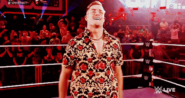 a man in a floral shirt stands in a wrestling ring with a crowd behind him
