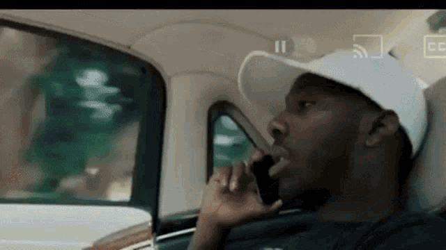a man wearing a white hat is talking on a cell phone in a car .