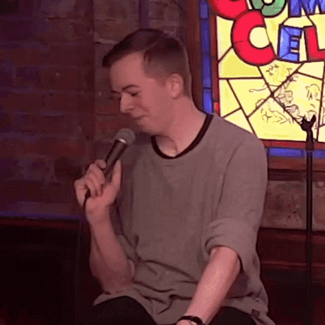 a man is singing into a microphone in front of a stained glass window with the letter c on it