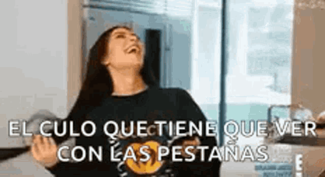 a woman is laughing and holding her hands up in the air while wearing a black sweater .