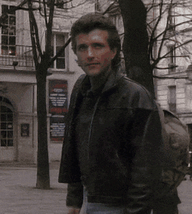 a man in a black leather jacket is standing in front of a building with a sign that says ' theatre ' on it