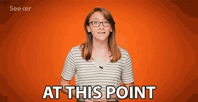 a woman wearing glasses stands in front of an orange background and says at this point