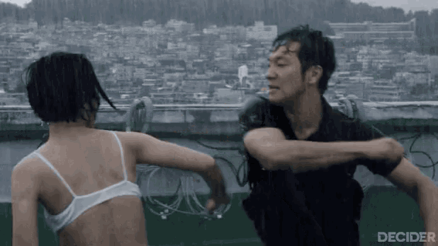 a man and a woman are fighting in the rain . the woman is wearing a white bra .