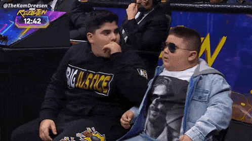 two boys wearing big justice shirts sit in the stands