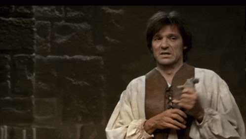 a man in a white shirt and brown vest is holding a hammer and says " cest carre carre chez vous bein "