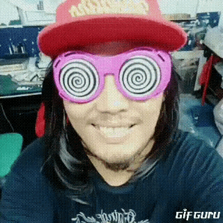 a man wearing a hat and pink hypnotic glasses is smiling .