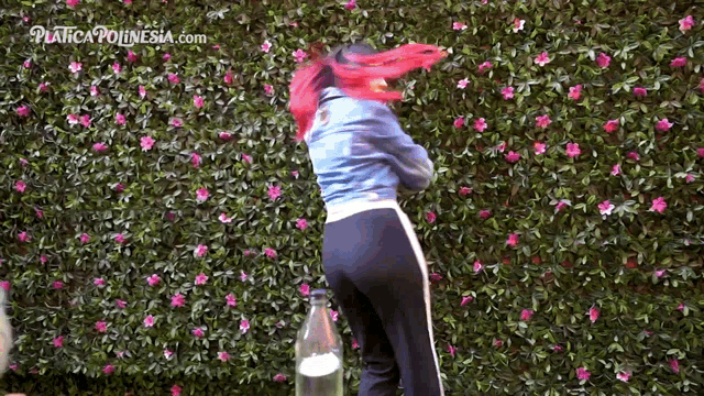 a woman with red hair stands in front of a wall of pink flowers