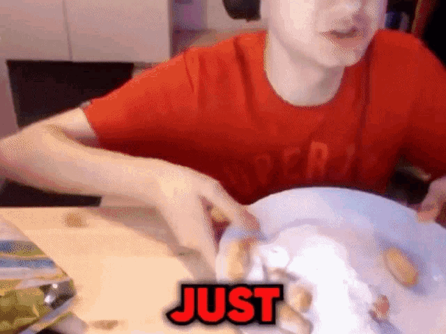 a man in a red shirt is sitting at a table with a plate of food and the word just written in red