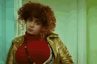 a woman with red curly hair is wearing a gold jacket and a red sweater .