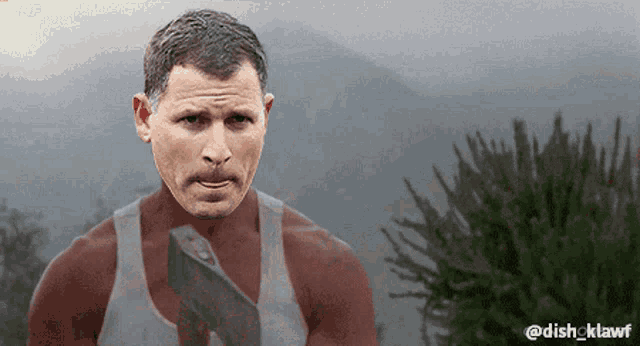 a man with a mustache is holding an axe in front of mountains