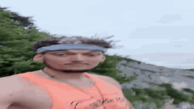 a man wearing an orange tank top and a blue headband is standing in the grass .